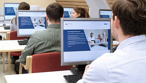 Mehrere Personen sitzen in einem Raum vor Computern und absolvieren den BKA Einstellungstest.