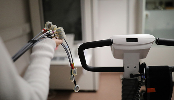Eine Hand voller Kabel und ein Ergometer für ein Belastungs-EKG in einem Behandlungsraum.