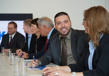 Frauen und Männer im Business-Look sitzen zusammen an einem langen Tisch