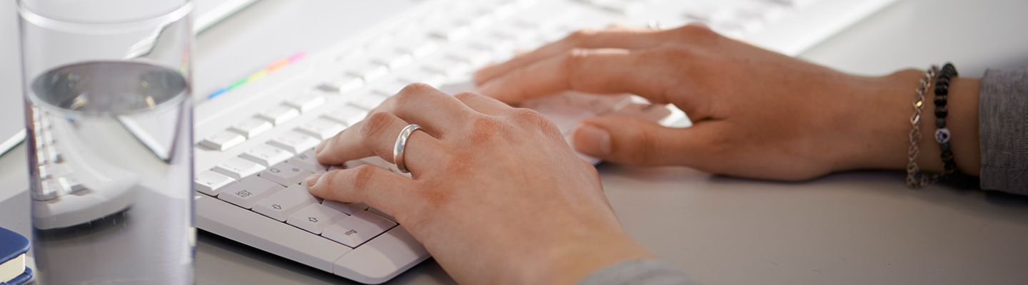 Zwei Frauenhände tippen auf einer weißen Computer-Tastatur